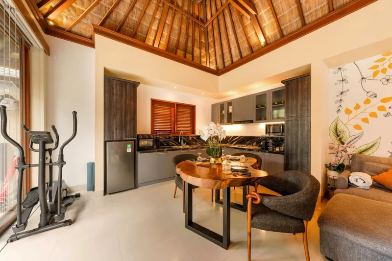 Kitchen and dining in Seminyak, Bali — dark marble splashback kitchen, live-edge suar wood dining table with orchid centrepiece, copper pendants, botanical mural beyond.