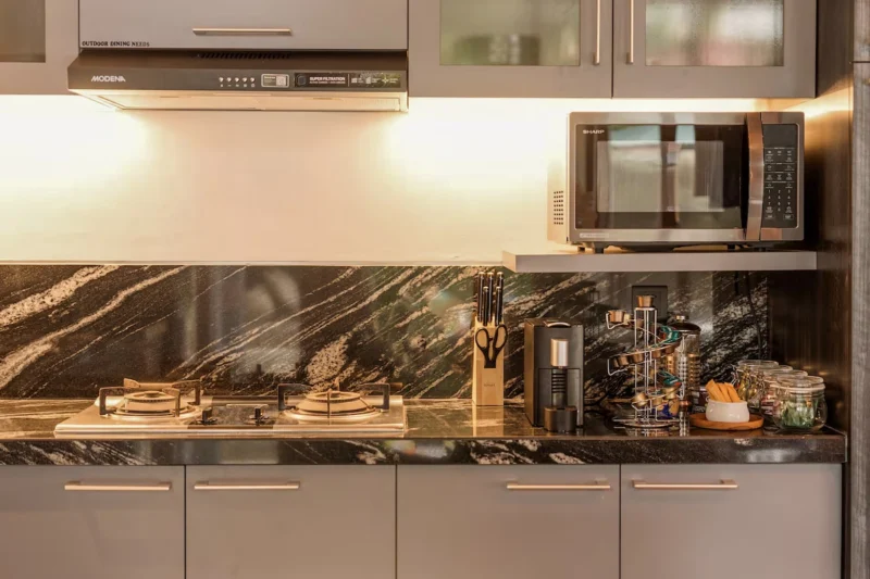 Kitchen bench detail in Seminyak, Bali — two-burner gas hob, Nespresso machine, knife block, Sharp microwave, dark black marble splashback with gold veining, grey cabinetry.