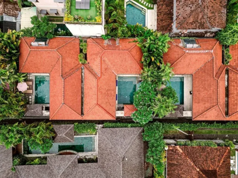 Aerial drone view of Disini Villas complex, Seminyak Bali — multiple private villas with terracotta rooftiles, individual private pools, dense tropical garden between each villa. Private compound layout.