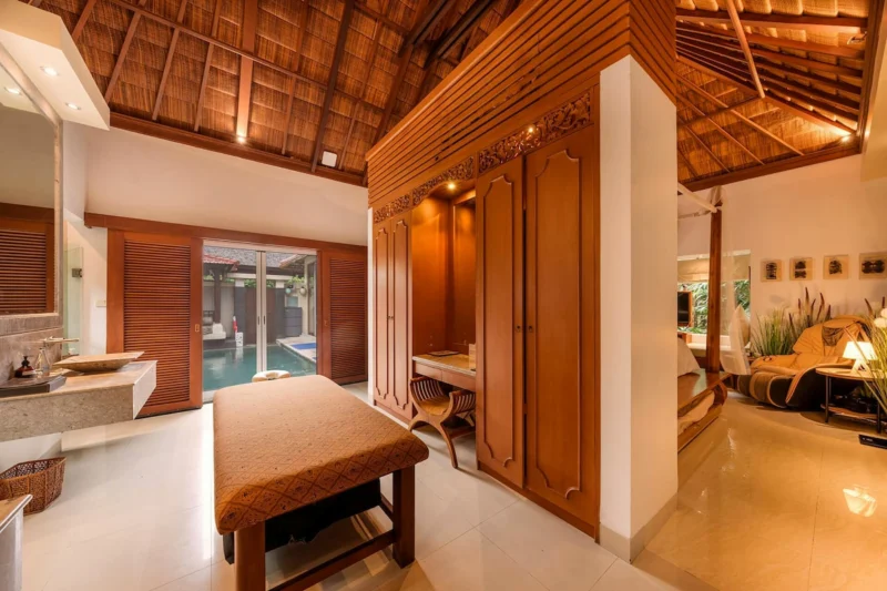 In-room spa and wellness space with massage table, carved Balinese teak wardrobe and alang-alang thatched ceiling – Seminyak, Bali