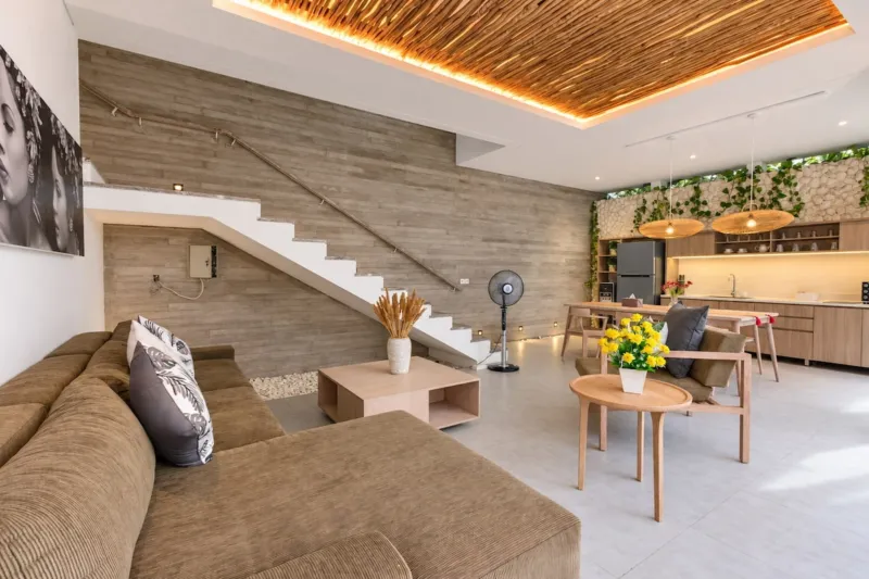 Villa Swan 01 — living, sectional sofa and open timber staircase under a thatched ceiling