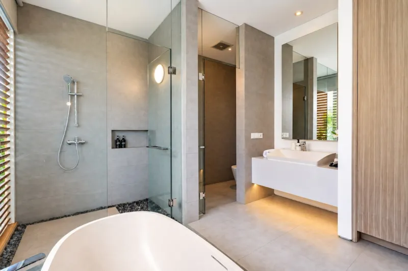 Villa Swan 01 — bathroom 1, glass-walled rain shower next to the freestanding bathtub and a stone vanity