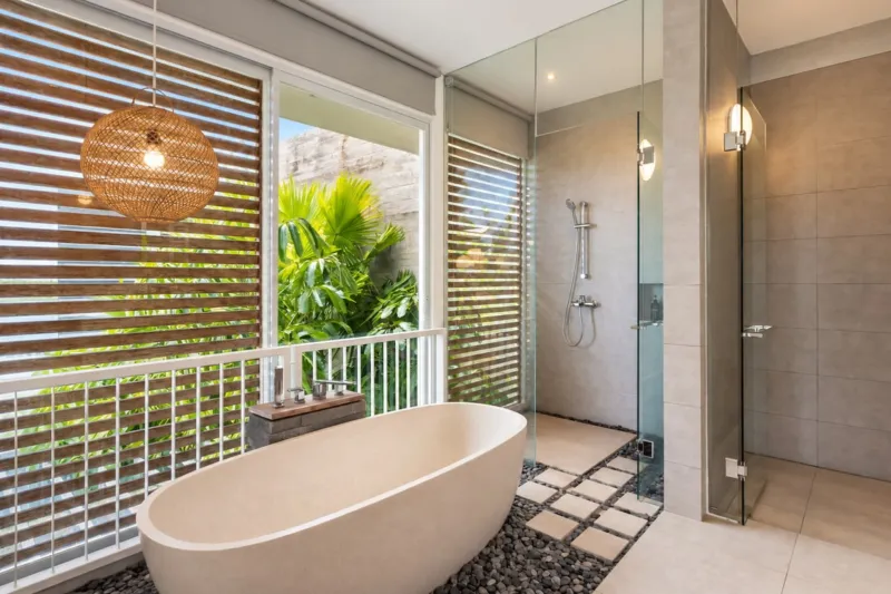Villa Swan 01 — bathroom 1, freestanding bathtub and glass rain shower beside a louvred window onto tropical planting