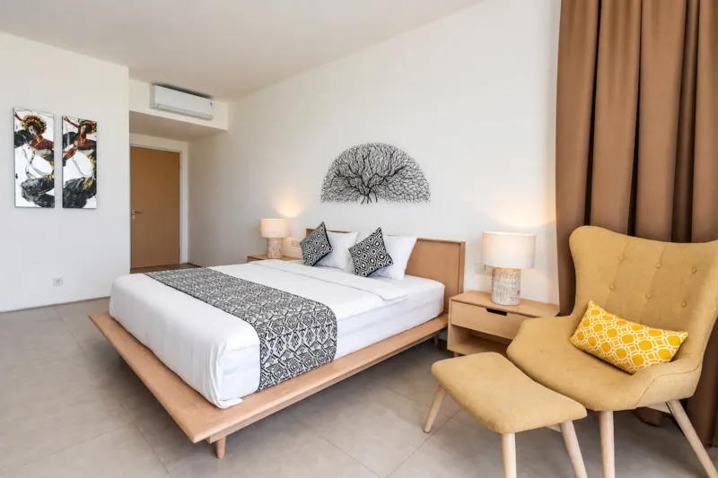 Villa Swan 01 — bedroom 1, king bed, mustard armchair and footstool under air conditioning