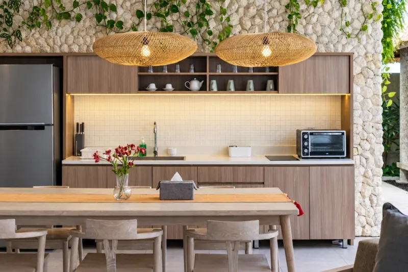 Villa Swan 01 — kitchen, timber cabinetry, open shelving and two woven rattan pendants against stacked stone