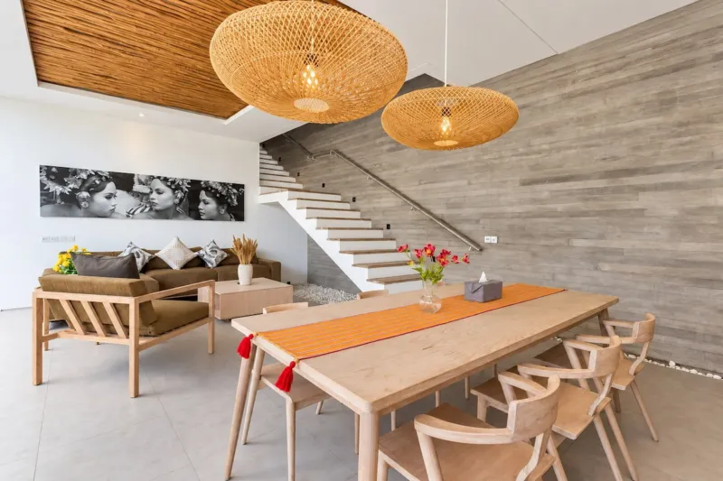 Villa Swan 01 — dining, timber table under two rattan pendants with the sofa and staircase behind